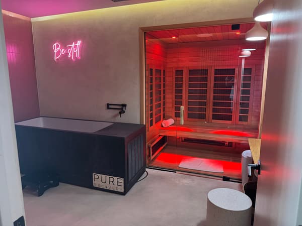 Pure Recovery suite with cold plunge, red infrared sauna, and Be Still neon sign