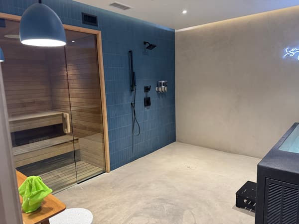 Pure Recovery suite with glass sauna, blue tile shower, and cold plunge under Be Still neon